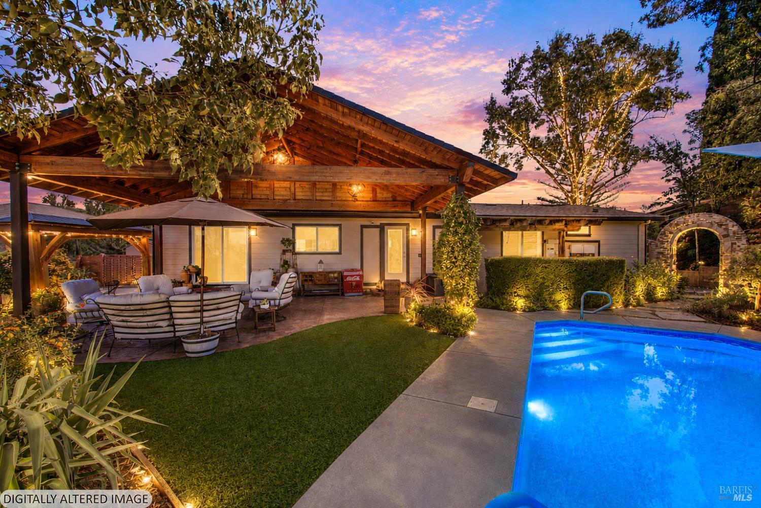 The covered outdoor living space with exposed wood beams, patio seating and the lit swimming pool at twilight